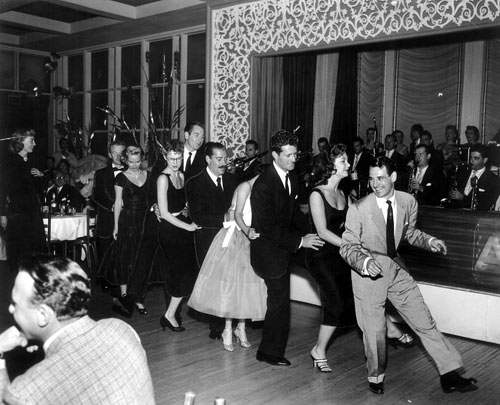 1950s Photo: Ray Anthony leads a group as they dance to his big hit of “The Bunny Hop” at Ciro’s. Behind Anthony is actress Mitzi Gaynor and Hugh O’Brian. Man with the mustache is comedian Jerry Colonna. Marie Windsor watches on the left.