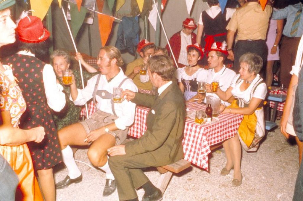 1960s/ 1970s vintage photo of a group of men and women in dirndls and lederhosen singing 'Ein Prosit' at an Oktoberfest party at the Concordia Club in Kitchener, Ontario Canada