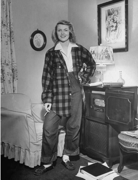 1940s vintage image of a young girl in a plaid oversize jacket, jeans and smoking in her livingroom beside the radio. 