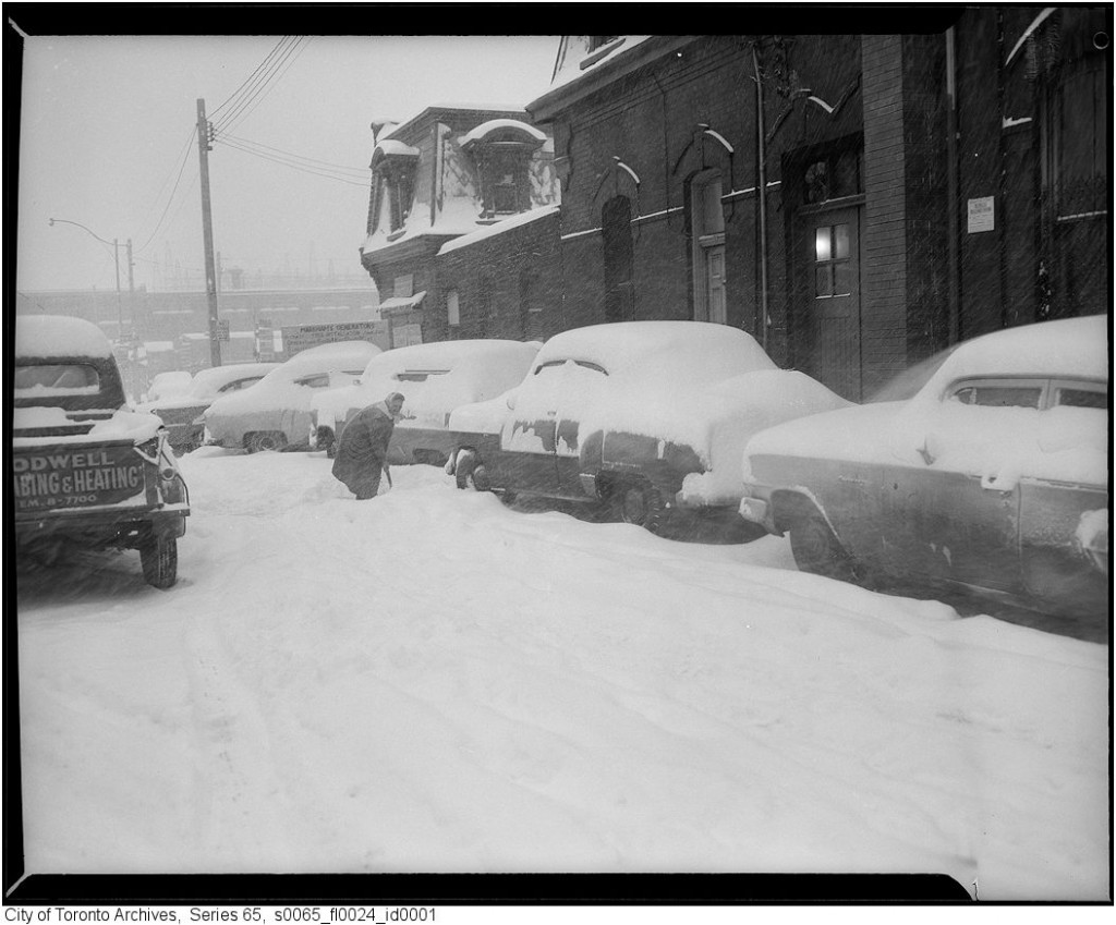 Vintage Photo of a Toronto Snowstorm in the 1950s or 1960s. Image features cars covered in snow and someone shoveling. 