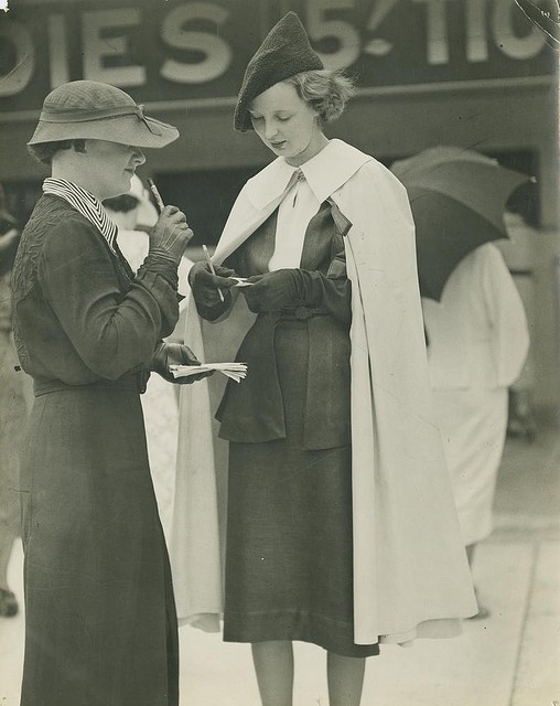 1930s racetrack fashion- 1930s vintage photo of two woman in 1930s fashions writing down their bets at the racetrack. 