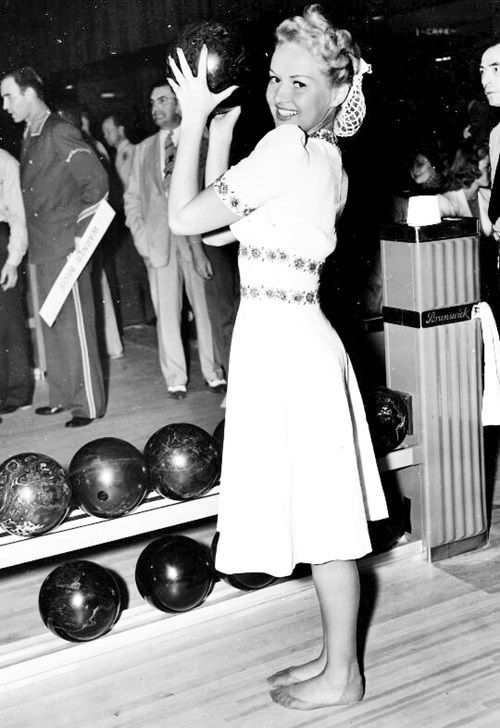 1940s vintage photo of a woman in 1940s dress, 1940s snood getting ready to bowl. Fun vintage bowling style. 