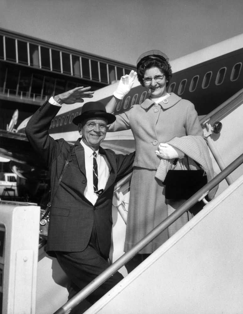 1960s vintage photo of an older couple waving from the steps of the plane. Stylish air travel plane. 