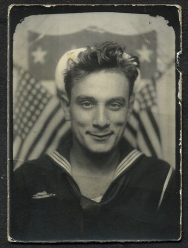 1940s vintage photo of a young handsome sailor posing for a photo in a photo booth. 