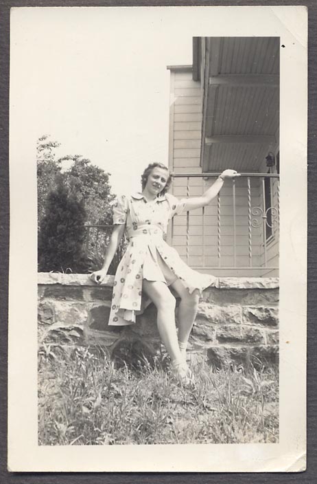 1940s vintage photo of a young woman in a two piece 1940s playsuit  posing for a photo on the side of her house. 