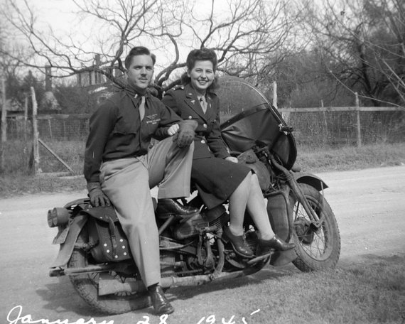 1940s vintage image of a wartime couple on a motorcycle. Both are wearing uniforms. 