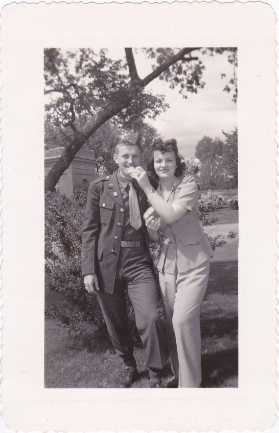 1940s vintage photo of a young woman and a young man in unifrom having fun together with a cookie. 