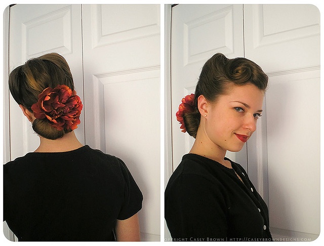 1940s hairstyle featuring victory rolls and a pin curl and hair flower.