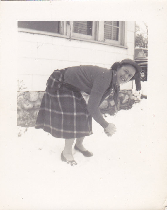 1940s woman in a plaid skirt in the winter getting ready to throw a snowball.