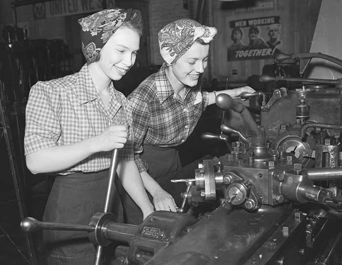 Working women in World War II working in a factory wearing hair scarves