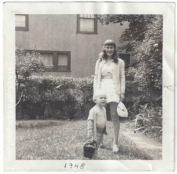 1940s vintage photo of a young mother with her child posing for a photo. The young woman is wearing 1940s shorts and 1940s crop top style top. Cute vintage summer style!