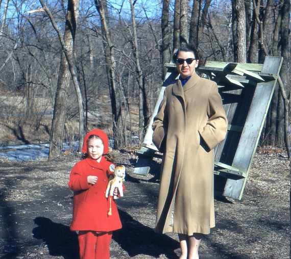 1950s vintage photo of a 1950s mom and daughter in winter coats posing for a photo outside. 