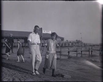 1920s vintage photo of a man and woman in 1920s fashions, Ellen and Fred on beach, Port Dover August, 1923 with the Summer Garden Dance Hall in the background. 