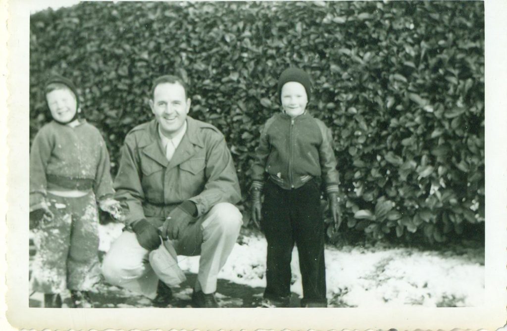 1950s vintage photo of a father posing with his two kids during the winter. 