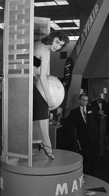 1950s vintage photo of a woman at a trade show holding a globe. 