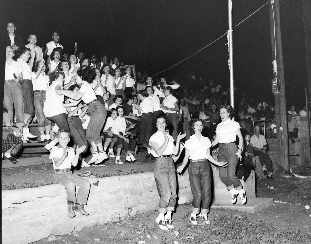 1940s vintage image of a bunch of teenager girls in jeans and white tops and saddles shops jumping around and having fun. 