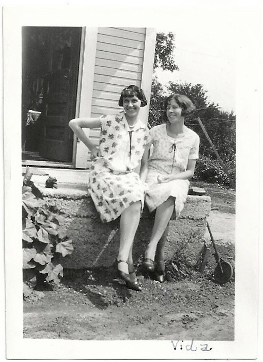 1920s vintage photo of two women in 1920s dresses and 1920s hairstyles posing in front of their house. 