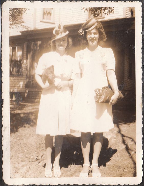 1940s vintage photo of 2 women in 1940s dresses and 1940s hats posing for a picture in front of their house. 