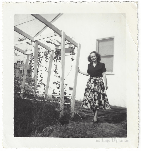 1940s vintage photo of a young woman in a patterned 1940s skirt and blouse posing beside a house. Super 1940s fashion.