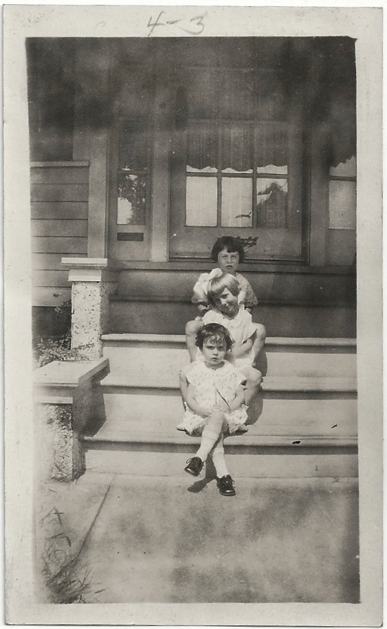 1920s vintage image of 3 young children posing in front of their house.