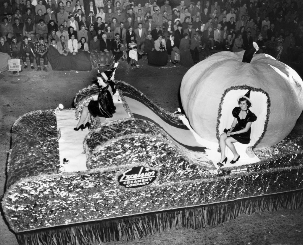 1950s vintage photo from an Anaheim Halloween Parade featuring a parade float with women as witches sitting with a pumpkin.