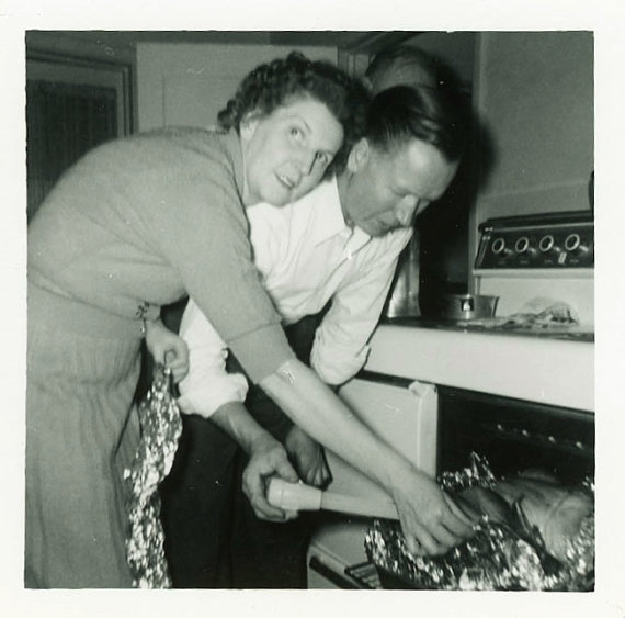 1950s vintage photo of a man and woman taking out the turkey of the oven. 