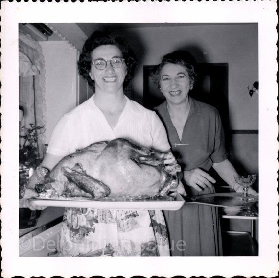 1950s vintage photo of two women in 1950s dresses posing with their Thanksgiving turkey they just took out of the oven. 