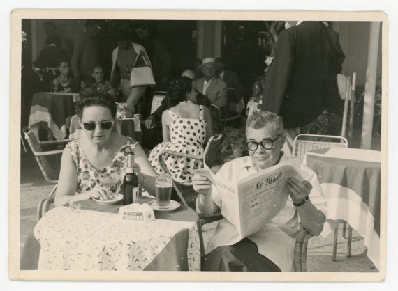 1960s vintage photo of a copule having a drink together and reading the paper in France. 