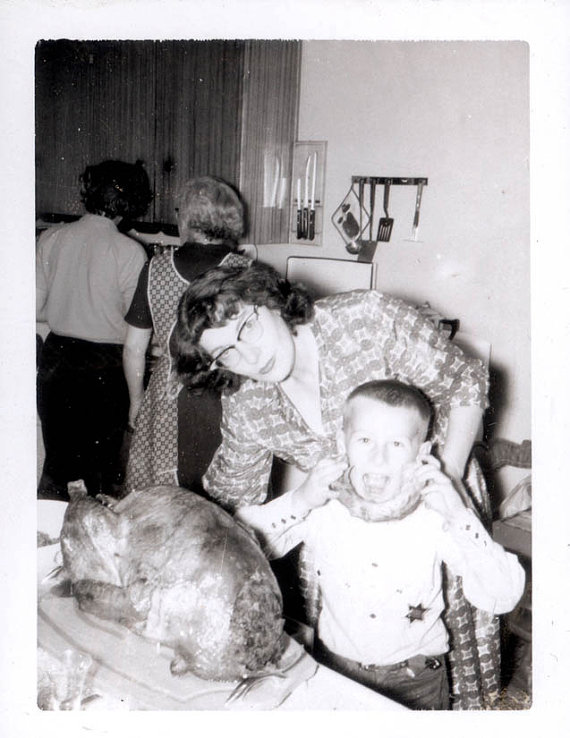 1950s vintage photo of a mom and her son on thanksgiving in front of the turkey. The kid has the neck. The mom is wearing cat eye glasses. 