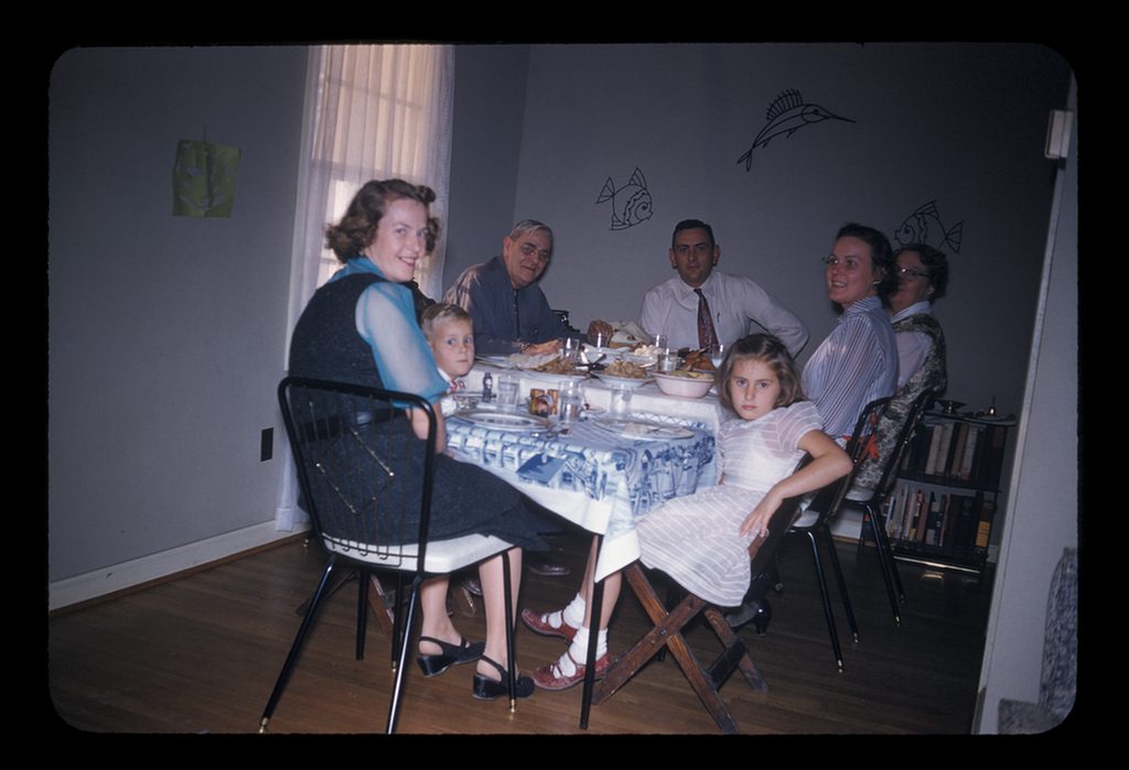 1950s vintage photo of a family sitting in a room with fish decor on the wall for Thanksgiving dinner in 1950s fashions. 