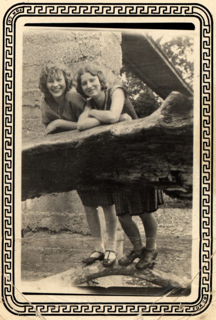 1920s vintage photo of two young girls (teens) having fun outside and posing together on a piece of wood. 