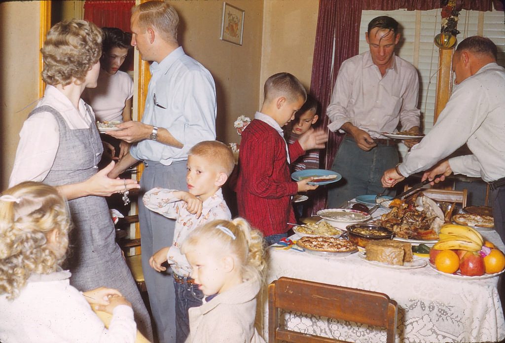 1950s vintage photo of a 1958 Thanksgiving family gathering featuring 1950s fashions and a table full of food. 