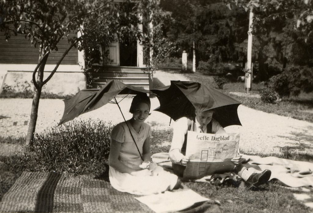 1930s vintage photo of a young couple with broken umbrellas holding them over themselves in 1930s fashions. 