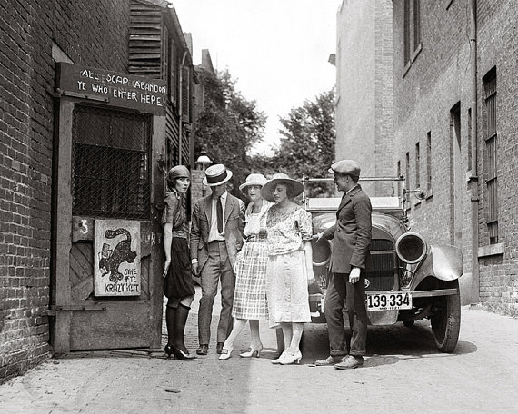 1920s Vintage Photo of men and women in 1920s fashions standing outside of a Speakeasy with their 1920s car. 