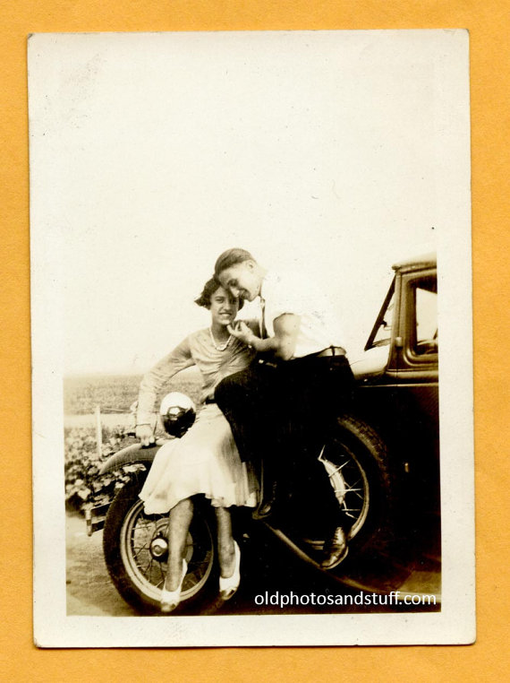 1930s vintage photo of a young couple sitting on a car joking with the camera