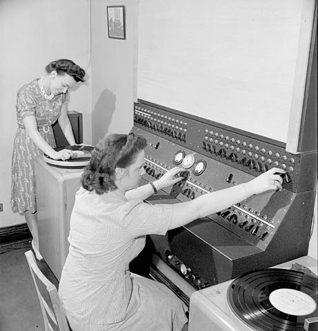 1940s vintage photo: ww2 canadian woman working for the war effort - picture is of 2 women workers selecting the music to be played from their central control room at a Montreal factory.