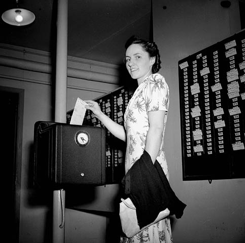 1940s vintage photo of a woman in a floral 1940s dress punching in to a time clock to do her job for the War effort in Canada. 