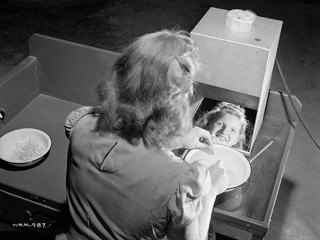 1940s vintage photo: ww2 canadian woman working for the war effort -Testing lenses, at the Instruments Division of the Canadian Arsenals Ltd. optical plant. Cute 1940s hairstyle. 