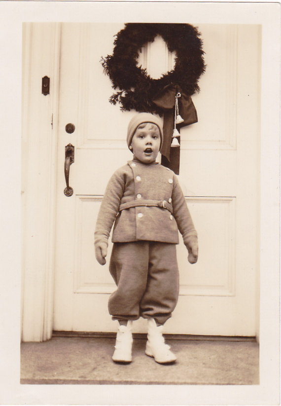 1930s Vintage photo of boy in winter snowsuit standing outsid eof a door with a Christmas Wreath on it.