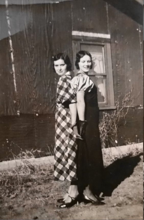 1930s vintage photo of two stylish young women in 1930s dresses posing together back to back. 