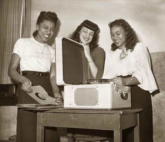 1940s vintage photo of three Black Women in 1940s fashions playing records on a record player.