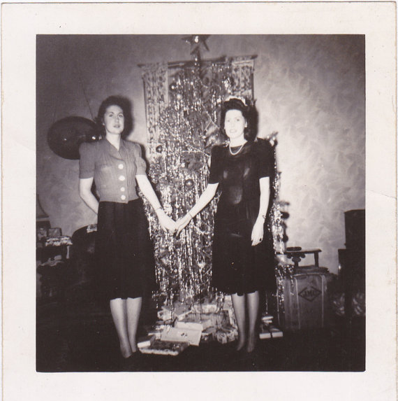 1940s vintage christmas image of two women in 1940s dress and 1940s skirt and sweater posing in front of their Christmas Tree all covered in Tinsel. 