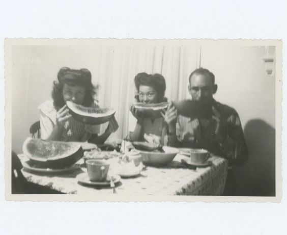 1940s vintage photo of women with 1940s hairstyles (victory rolls) and one man eating watermelon.