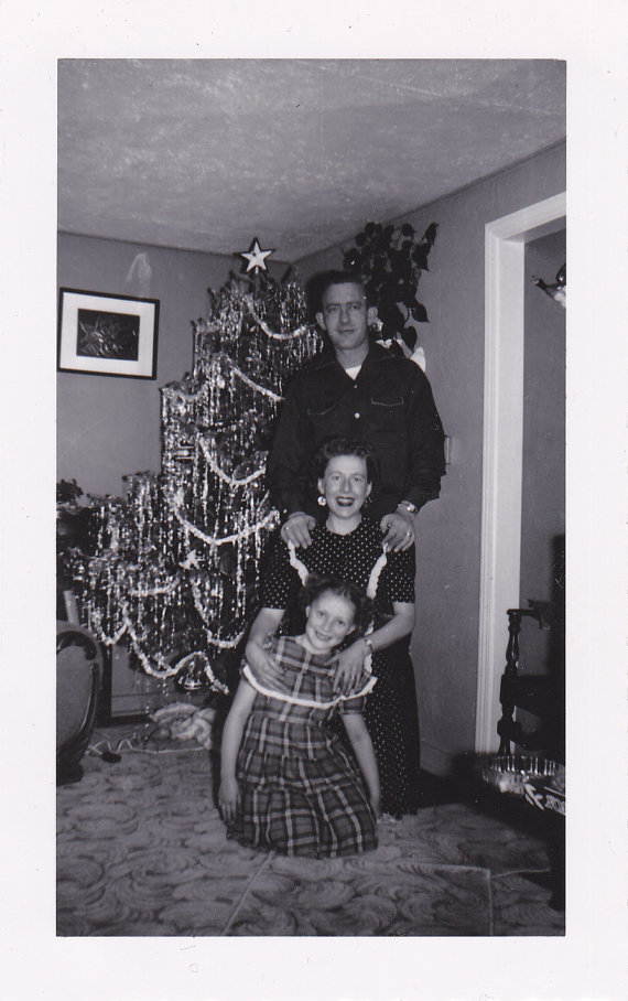 1950s photo of a family with tinsel tree posing together in front of their Christmas Tree. 