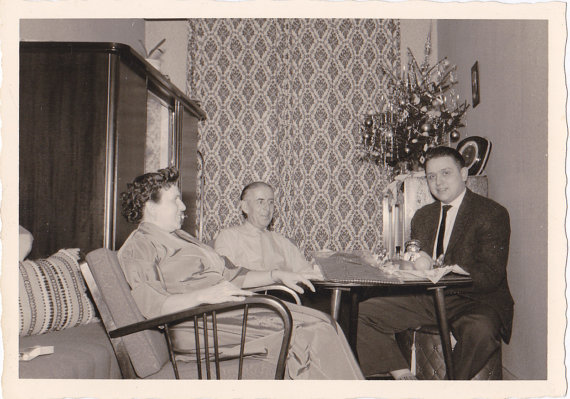 1950s vintage image of a family in a very small room with a small Christmas tree in the corner enjoying time together. 