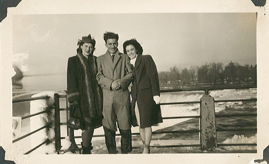 1940s vintage photo of two women and a man in 1940s winter fashions posing beside Niagara Falls. 