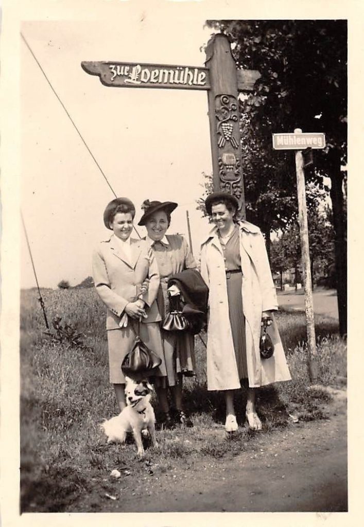 1940's black and white photo of women and their dog in 1940s fashions posing together.