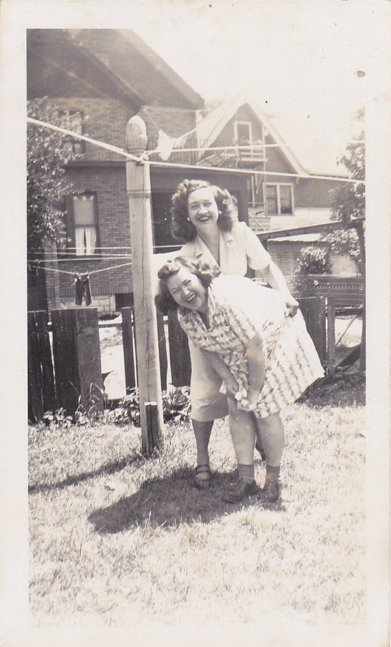 1940s vintage image of 2 women laughing in 1940s dresses and stunning 1940s Hairstyles. 