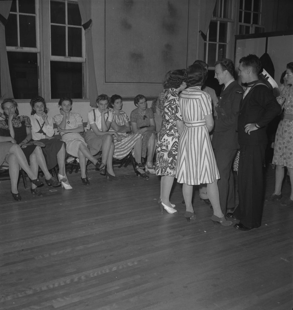 1940s vintage image of a group of women in 1940s fashions sitting on the side at a dance. 