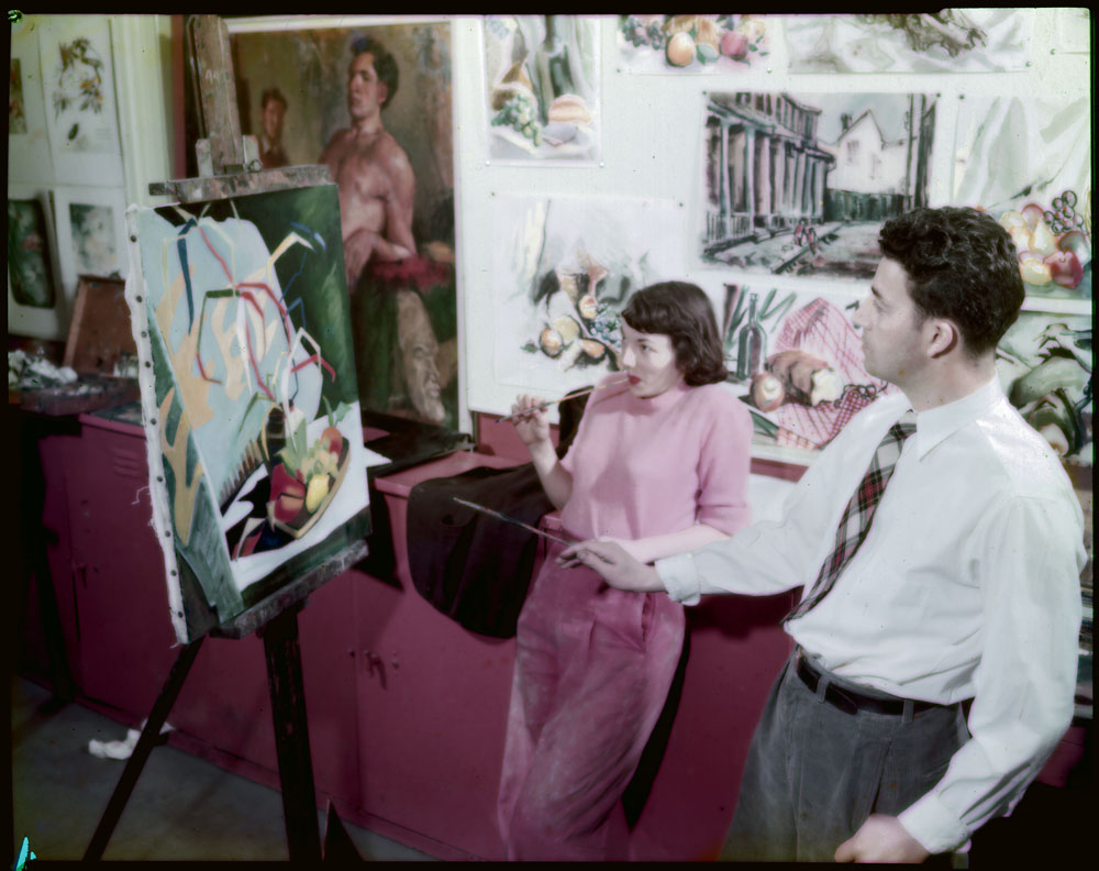 1940s vintage photo of students in art class studing a painting. October 1949: Paul Macdonald of Gananoque, Ont, 3rd year drawing and painting student, paints semi-abstract still life with fruit while 2nd year ceramics student Nancy Snider, of Islington, Ont, watches.